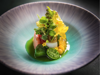 A close-up of a colourful fine dining fish dish with green tomatoes and edible flowers, arranged in a beautiful bowl