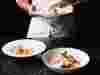 A chef with three white bowls of food all against a black background