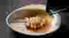 A green jug pouring sauce over an abalone skewer in an irregularly-shaped white bowl