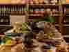 Table heaped with fresh Mexican produce, with racks of bread loaves in the background