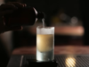 A person pouring a pale yellow cocktail into a chilled tumbler in a darkened room