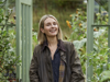 Kate Harvey against a background of foliage with orange flowers and a greenhouse doorway