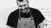 Black and white image of Chef James Sherwin of Wild Shropshire, laughing in front of brick wall