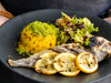 Hands holding plate with whole fish, salad leaves and yellow rice