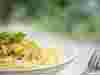 Close up shot of white bowl of spaghetti with yellow courgette, with fork to the right