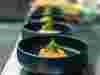 Dark ceramic bowls with salmon and herbs, lined up on the pass at a restaurant