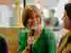 Ceri Gott in a green dress holding a microphone and speaking with Juliane Caillouette Noble