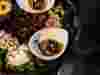 Beautifully presented food in small white bowls surrounded by foraged plants