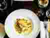Overhead shot of fish dish with clams on a wooden table with a glass of white wine