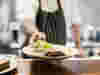 Chef in striped apron holding a plate of food out towards the camera