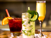 Three different cocktails on a bar counter. A red drink in a rocks glass, a green herby drink in a highball glass and an orange drink in a flute.