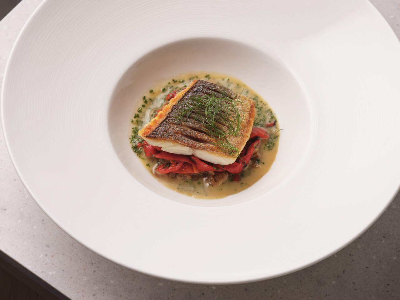 Piece of white fish with crispy skin on vegetables in wide-rimmed white bowl