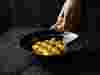 A hand pouring a jugful of sauce into a dark bowl of vibrantly coloured food